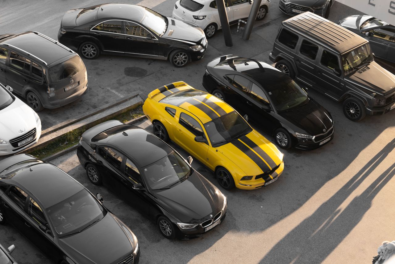 Home Top view of various cars parked in a parking lot, featuring a yellow sports car.