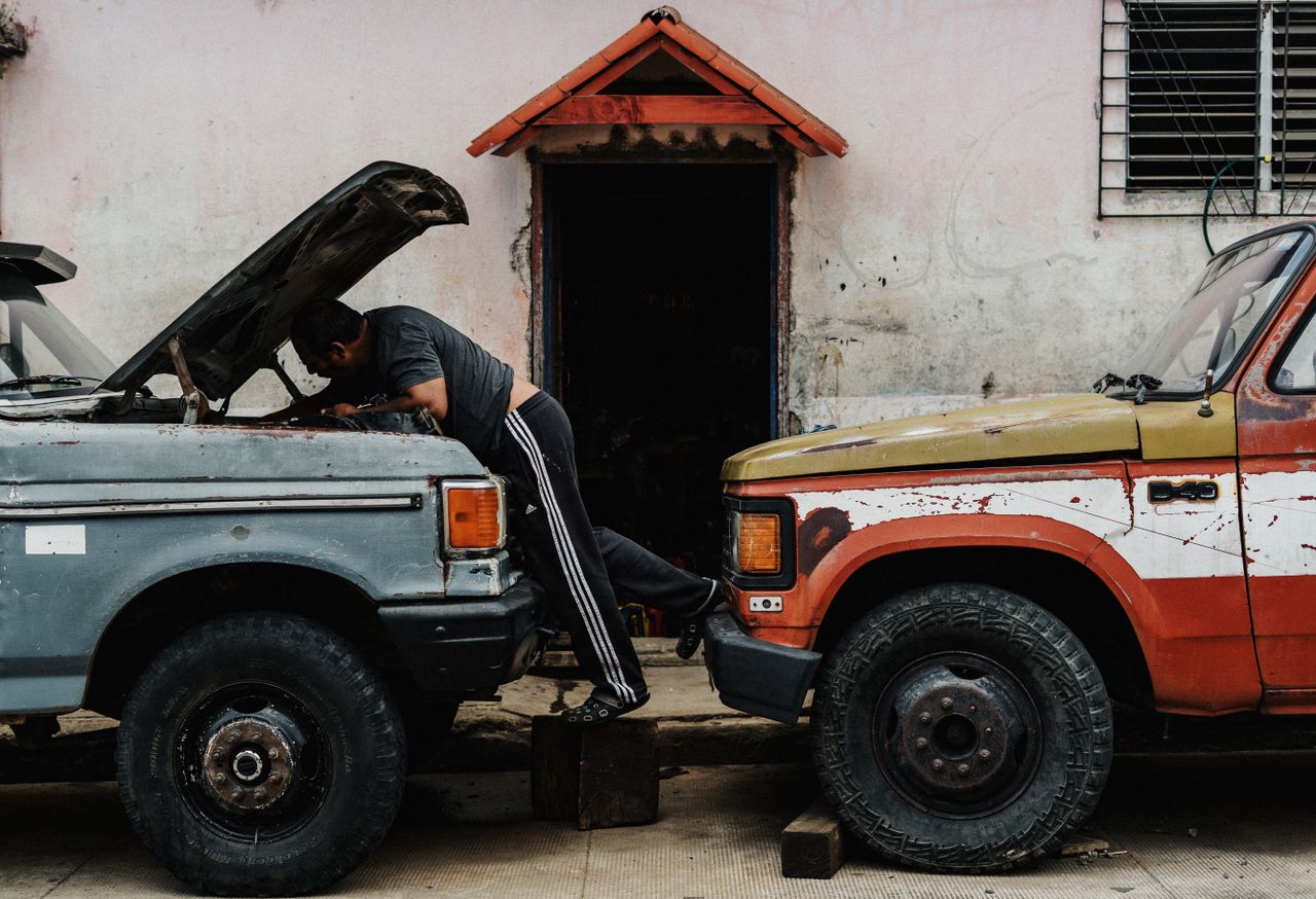 Home Mechanic working on vintage trucks in an urban setting, highlighting a candid street scene.
