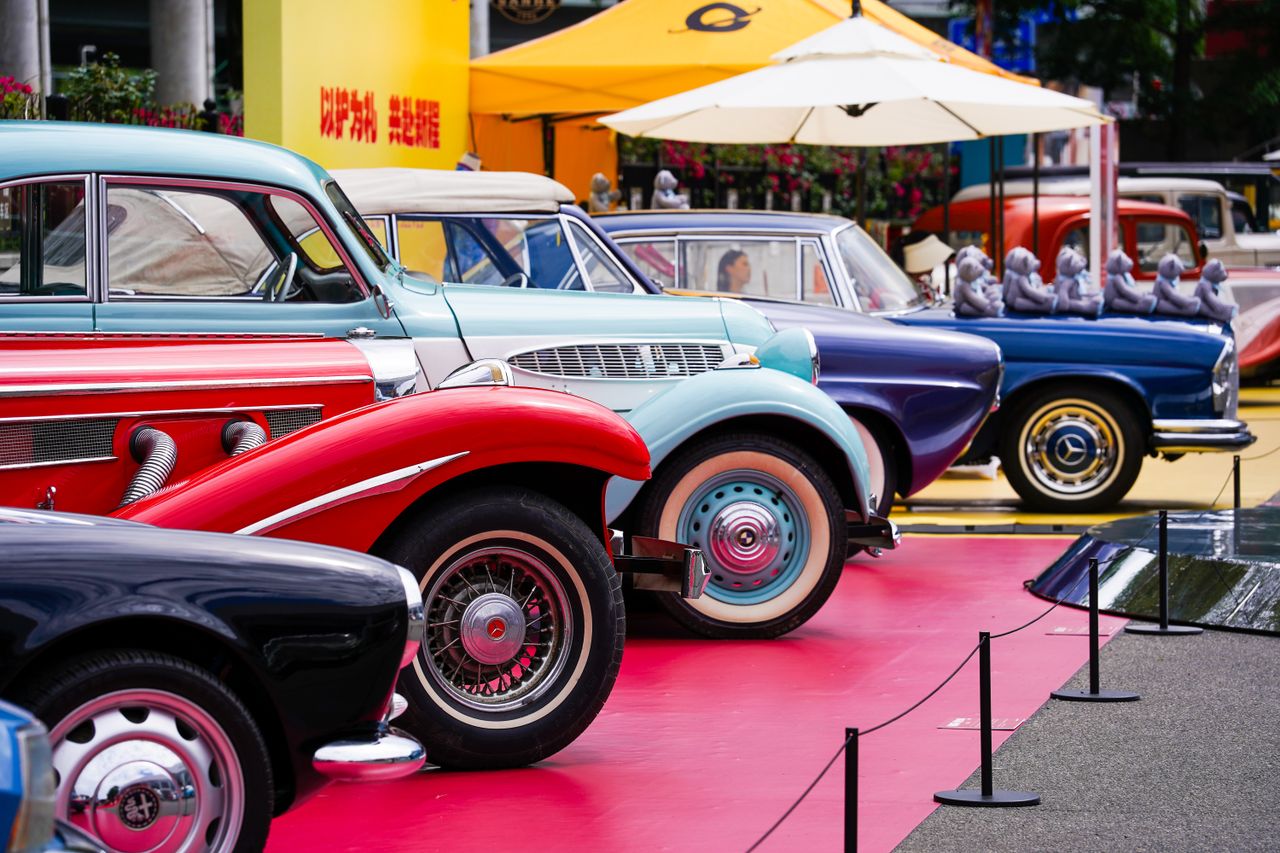 Home A row of colorful vintage cars showcased at an outdoor auto exhibition.